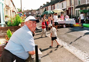 Older resident leaning on a garden wall observing a street party